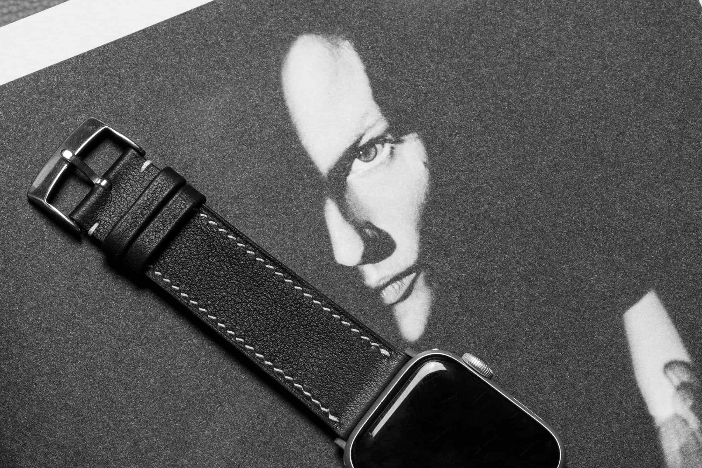 Black leather Apple Watch strap styled over a black-and-white editorial magazine spread, produced by AKC in Vietnam