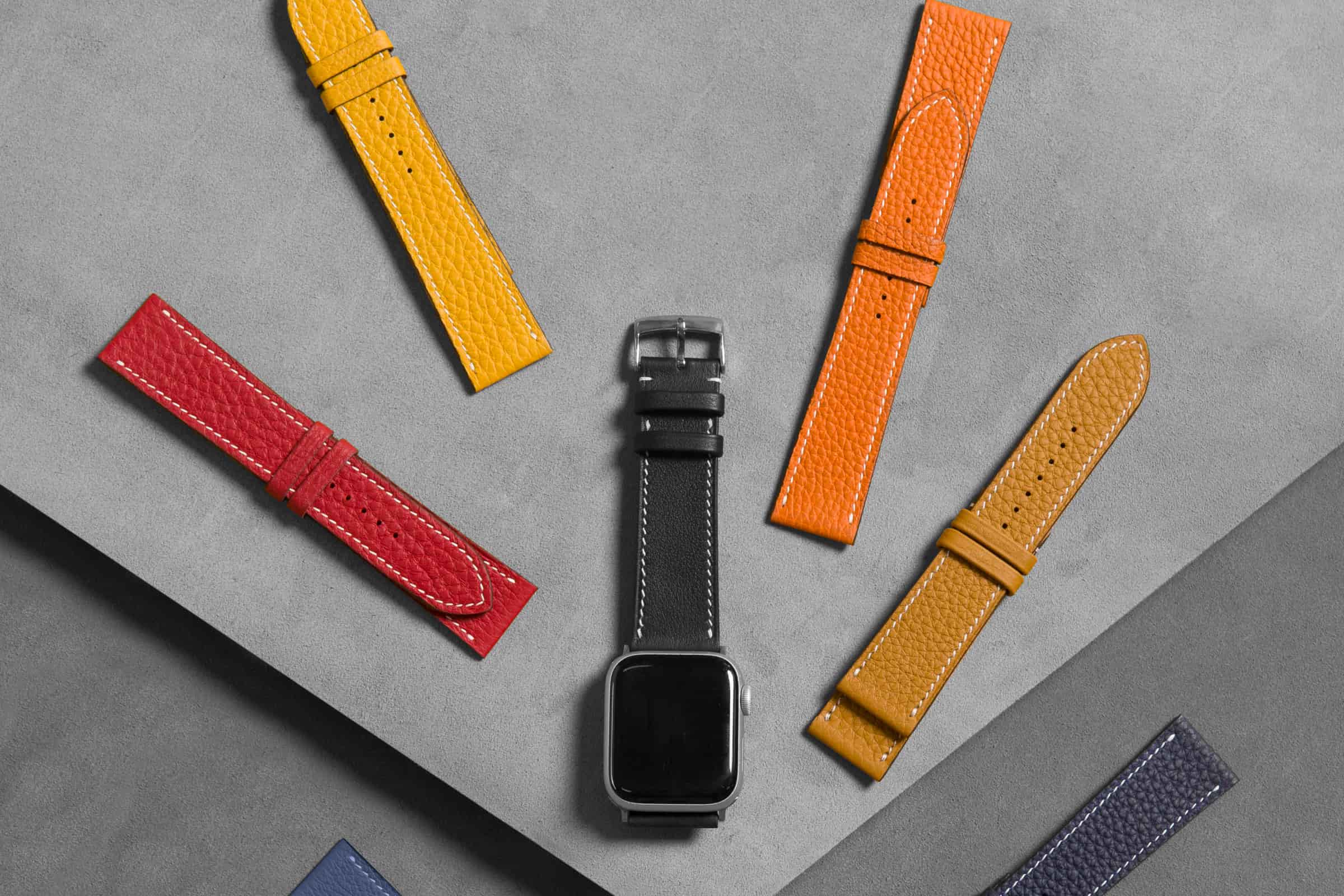 Seven dyed calf leather watch straps fanned around a wristwatch, showing contrast and tonal stitching options from AKC