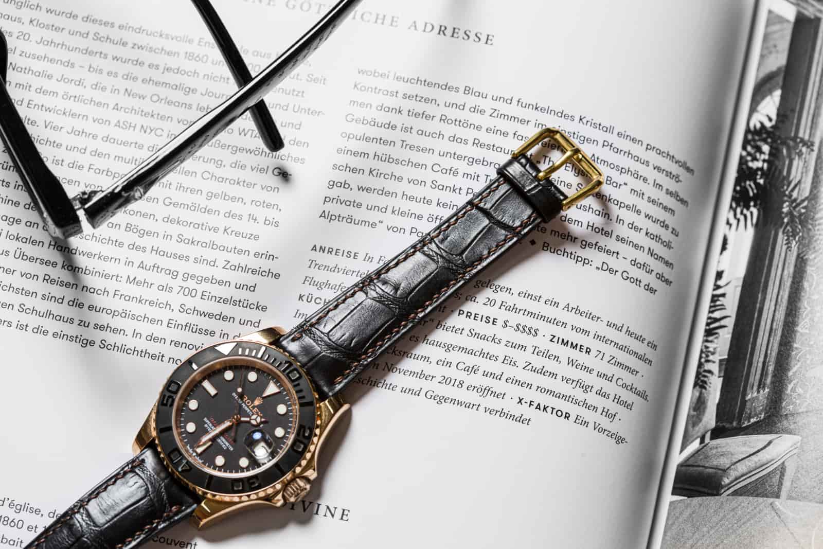 Grey alligator leather watch strap laid across a magazine spread, the scale run legible from lug to tip, made by AKC