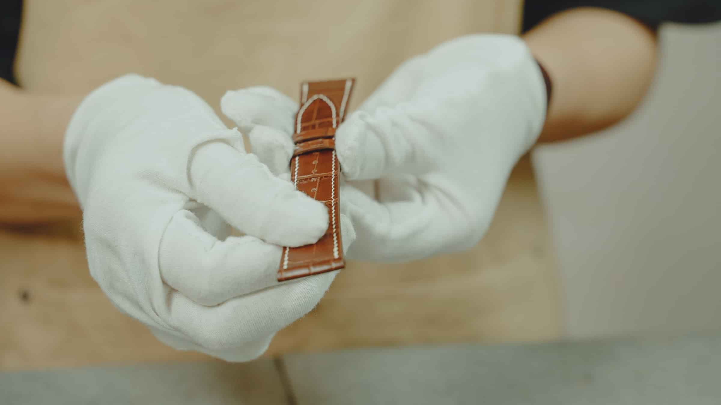 An AKC inspector in white gloves examining a finished leather watch strap before packing